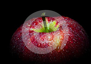 Water droplet on glossy surface of red apple on black background