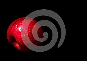 Water droplet on glossy surface of red apple on black background