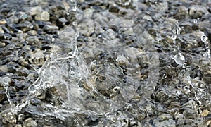 Water droplets falling into the small pool of water covering small stones creating intricate splash patterns