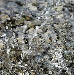 Water droplets falling into the small pool of water covering small stones creating intricate splash patterns