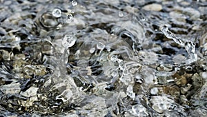 Water droplets falling into the small pool of water covering small stones creating intricate splash patterns