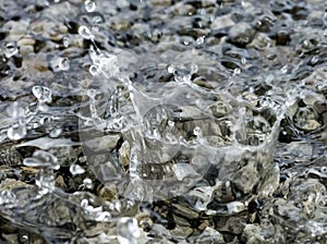 Water droplets falling into the small pool of water covering small stones creating intricate splash patterns