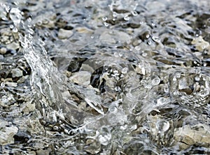 Water droplets falling into the small pool of water covering small stones creating intricate splash patterns