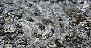 Water droplets falling into the small pool of water covering small stones creating intricate splash patterns