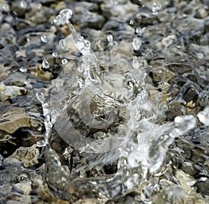 Water droplets falling into the small pool of water covering small stones creating intricate splash patterns