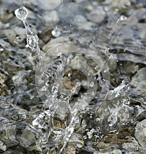 Water droplets falling into the small pool of water covering small stones creating intricate splash patterns