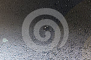 Water droplets on the glass glisten in a beam of light on a black background, close-up texture