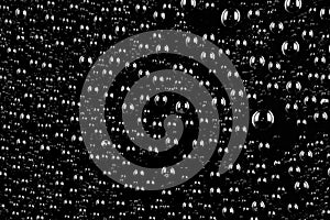 Water drops on a black plastic, glass surface.