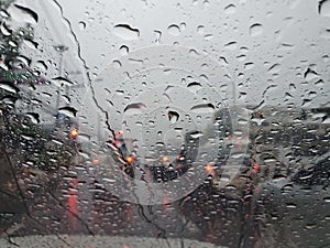 Water drops in front of car mirror with blur traffic on road in raining day