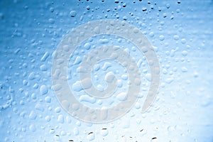 Water drops on glass with blurred blue sky background , rain in the city.