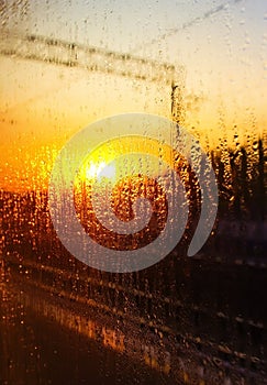 Water drops on the glass of the train on the background of the setting sun railroad