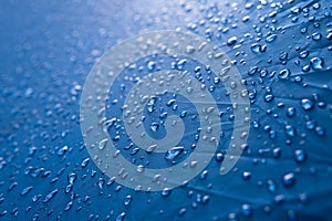 Water drops on waterproof nylon fabric. Macro detail view of texture of blue woven synthetic waterproof clothing. morning dew on