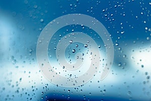 Water drops on the window, blue sky and clouds in the blurry background