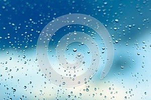 Water drops on the window, blue sky and clouds in the blurry background