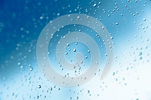 Water drops on the window, blue sky and clouds in the blurry background