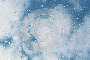 Water drops on a window glass, a blue cloudy sky at the background.