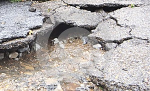 Water erosion of the road and red car. Broken asphalt background. Danger hole, stone gray backdrop