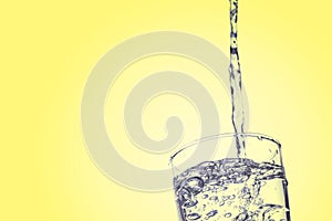 Water falling in glass on yellow background