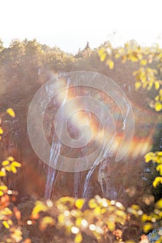 Water that falls from a large waterfall over stone slopes with sunbeams, Plitvice Lakes