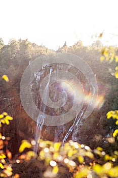 Water that falls from a large waterfall over stone slopes with sunbeams, Plitvice Lakes