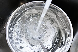 Water from faucet splashing into a stainless steel bowl and spoon thats have just been used to whip egg whites - sitting in a stai photo