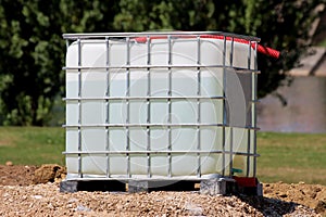 Water filled white intermediate bulk container or IBC plastic tank with metal cage put on top of gravel pile at construction site