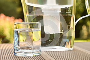 Water filter pitcher and a clean glass of a clear water close up on the summer garden background