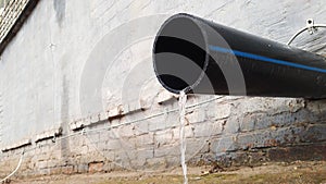 Water flow from black plastic drain pipe on an industrial building after rain