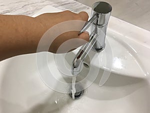 Water flow from metal tap inside basin by woman hand in bathroom.