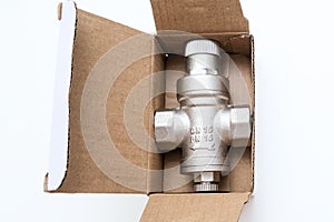 Water flow regulator, pressure reducer valve in a carton box on white background, new repair part for plumbing, water