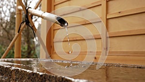 Water flowing from bamboo pipe faucet in traditional Japanese mini garden.
