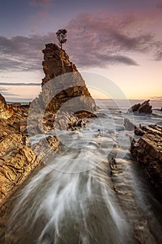 Water flowing fast through narrow chasm beside seastack woth sol