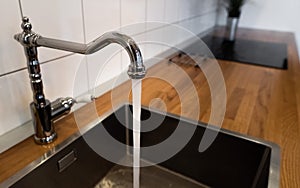 Water flowing out of a kitchen stainless steel tap into the sink. Water misuse in domestic duties and activities. Overusing