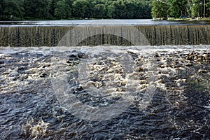 Water Flowing Over A Dam With Forest and Lake in the Background