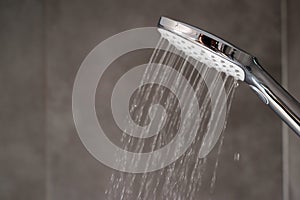 Water flowing from shower, close up. Modern bathroom interior. Chrome shower head with splashing water