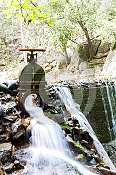 The water flowing from the steel drain into the brook of the waterfall in the tropical forest.