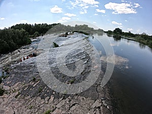 Water flows through the dam of Mygiivska HPP. Rapids and river dam on the Southern Bug. Group of people resting on the river water