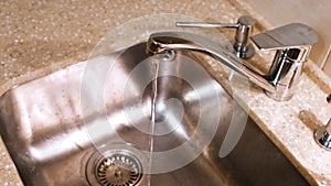 Water flows from the kitchen faucet into the metal sink. Concept. Clean water flowing from a chrome tap in the kitchen.