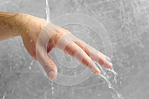 Water flows through the man`s hand on grey background. Hand close-up. photo