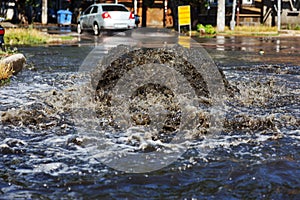 Water flows out of road sewage hatch. Drainage fountain of sewage. Accident of sewage system. Dirty sewage water flows fountain on