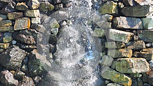 Water flows over the stones. Decorative outdoor fountain. A splashing stream of water flows over rough large stones