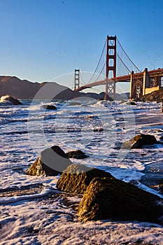 Water frothing around boulders in water at sunset with Golden Gate Bridge