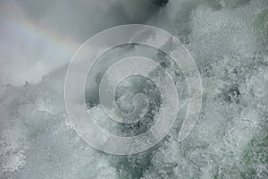 Water frothing from a waterfall with a faint rainbow.