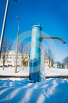 Water froze on the drinking column, blue water pump covered with ice, water well ice