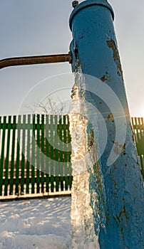 The water froze on the drinking column, water well ice, blue water pump covered with ice