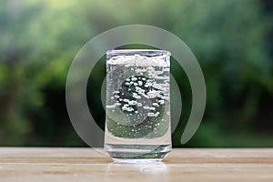 Water glass on wooden table outdoors and green background