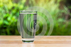 Water glass on wooden table outdoors and green background