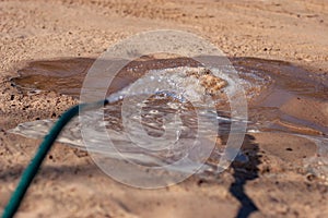 Water from a hose flows on sand in sunny weather.
