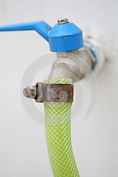 Water hose with rusty tightener with blue handle on white wall