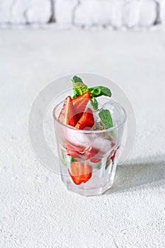 Water with ice, strawberry syrup, fresh strawberries and mint in a glass cup on a white background.